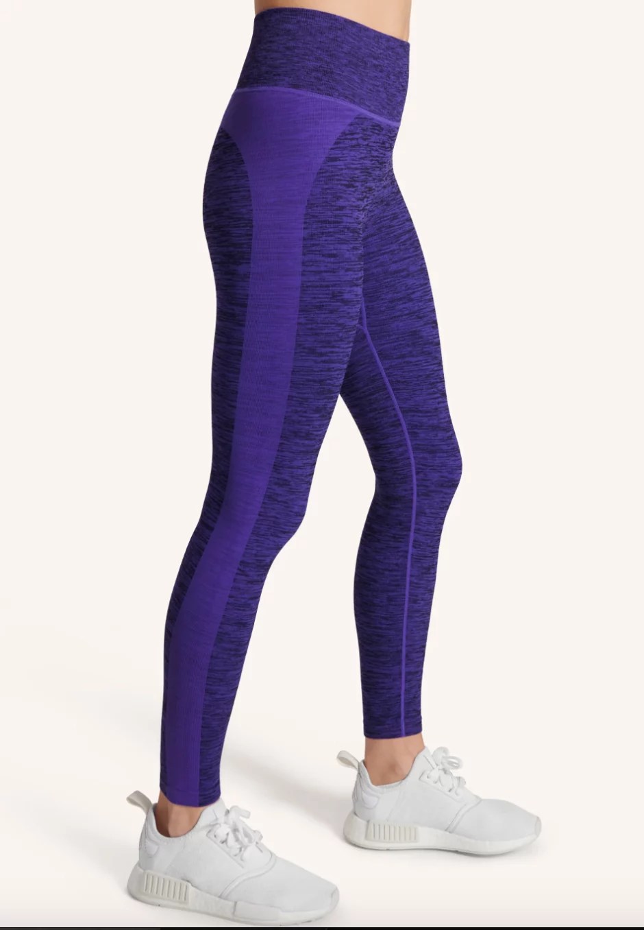 A model's lower body showing a pair of purple ankle length leggings with white sneakers.