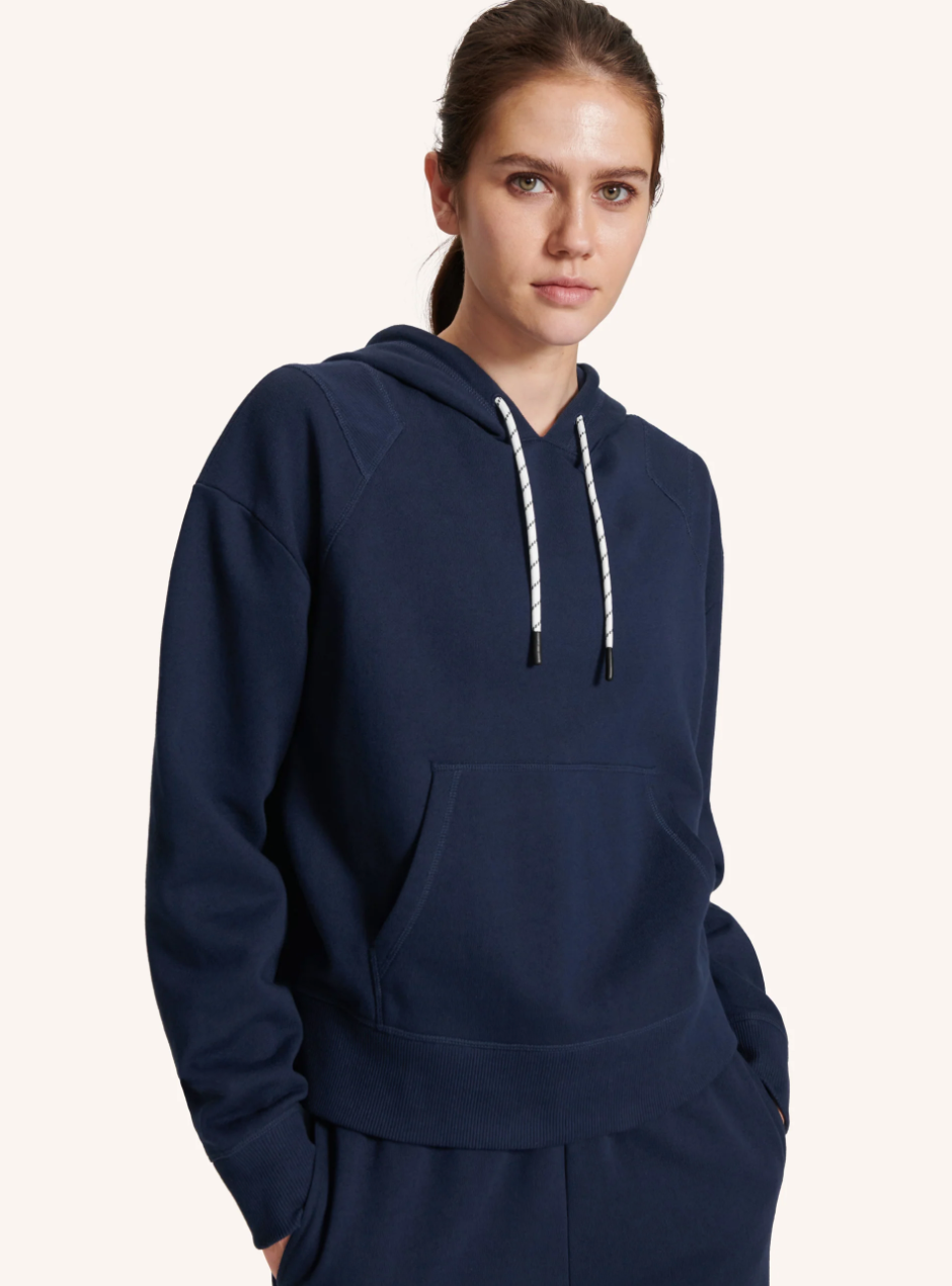 A model wearing a navy hoodie with white drawstrings at the neck.