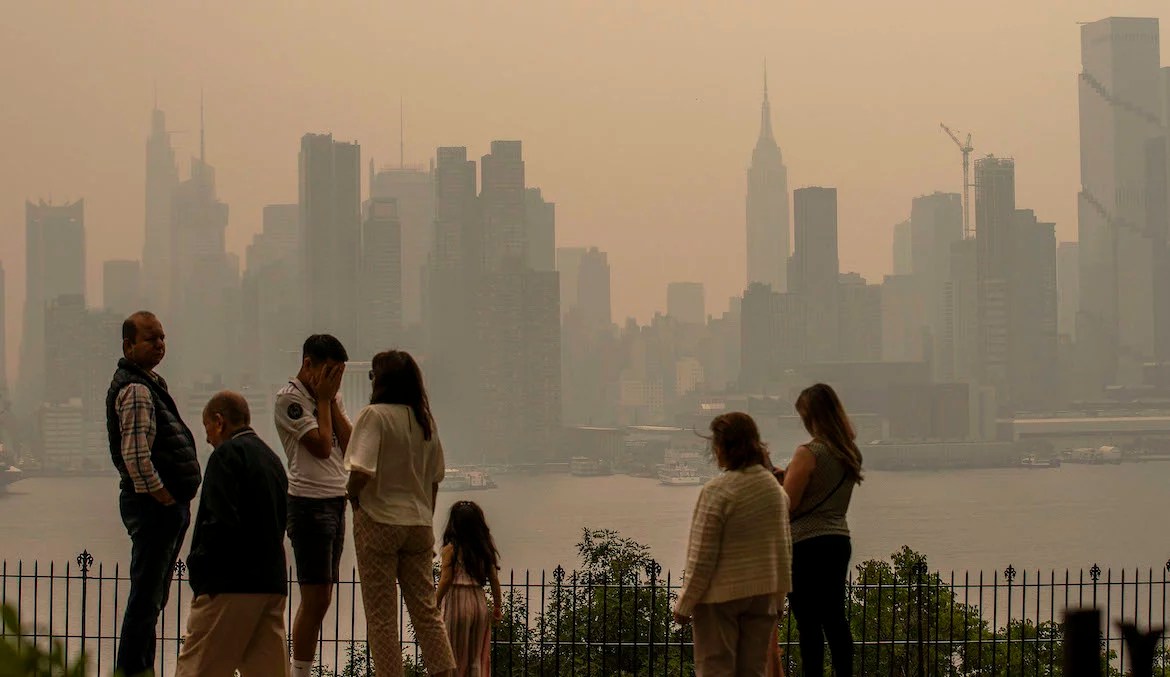 People standing in a park looking at an ashy, orange New York City skyline.