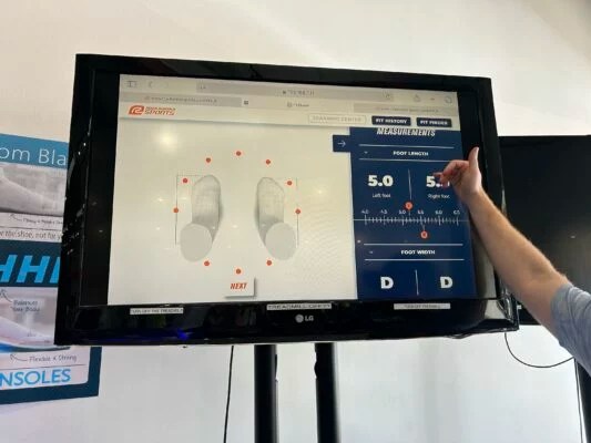 A monitor showing a 3D model of feet with a hand gesturing to the contents of the screen.