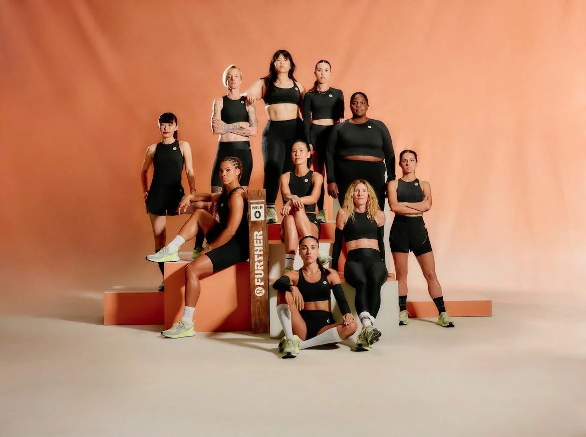 A group of women in black running clothes on a peach background.