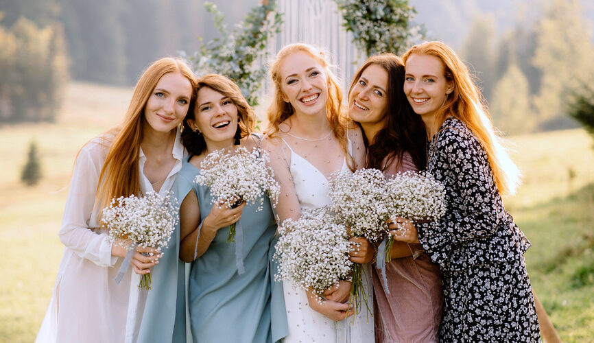 A group of women in wedding guest dresses smile while standing next to a bride.