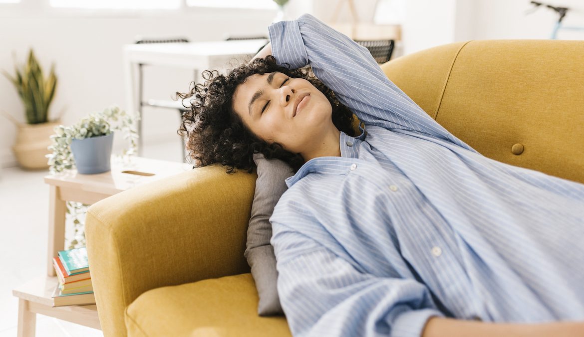Smiling young woman with eyes closed napping on sofa at home
