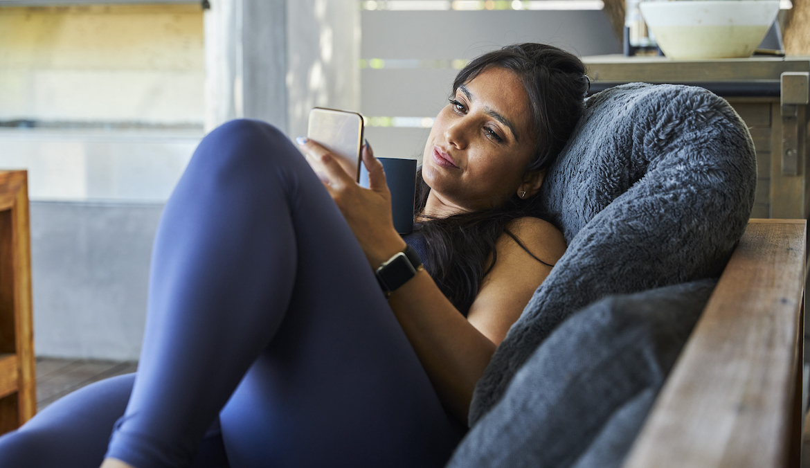 Woman using mobile phone while lying on sofa at home