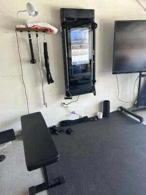 A Tonal home gym set-up in a garage, with a shelf, a bench, and accessories including a foam roller and weight belt.