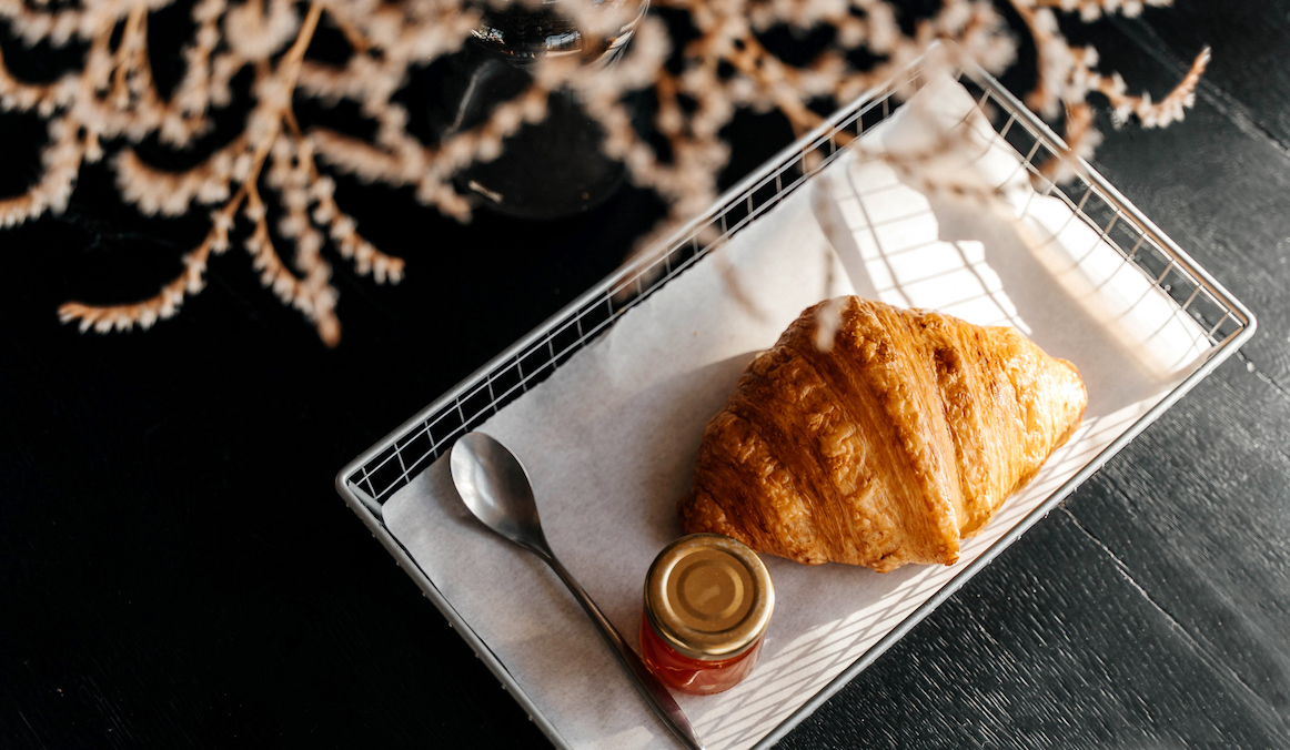 croissant with a jar of jam on a black wooden table