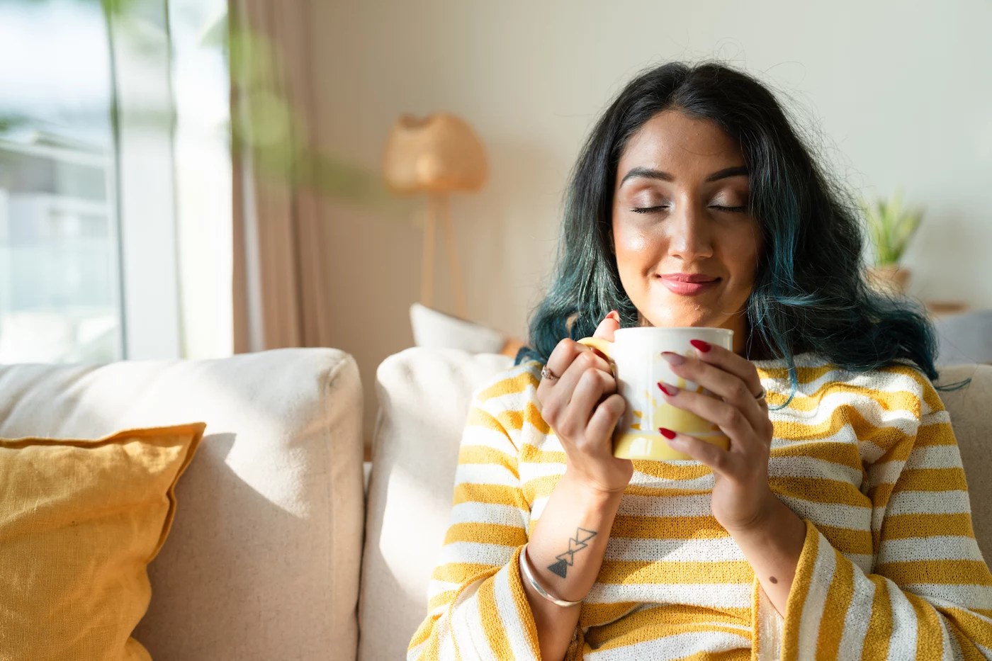 Woman drinking a cup of coffee on her couch. Find out the best spices to add to coffee