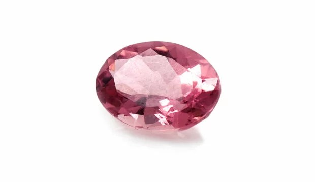 A pink tourmaline—one of the October birthstones—against a white backdrop.