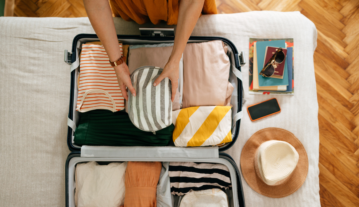 Shot from above of an anonymous woman packing things in her suitcase on the bed