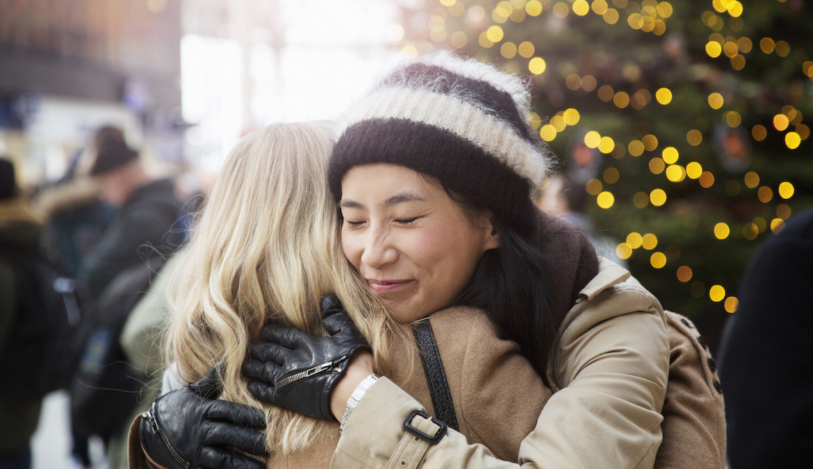 Two women hug in front of a Christmas tree.