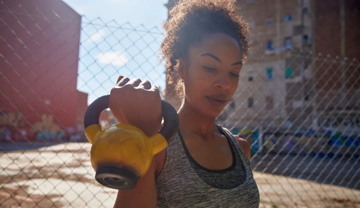 A woman holding a yellow kettlebell by her shoulder as part of a full-body kettlebell workout