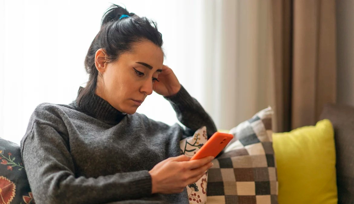 Woman sitting on a sofa and looking at mobile phone screen at home.