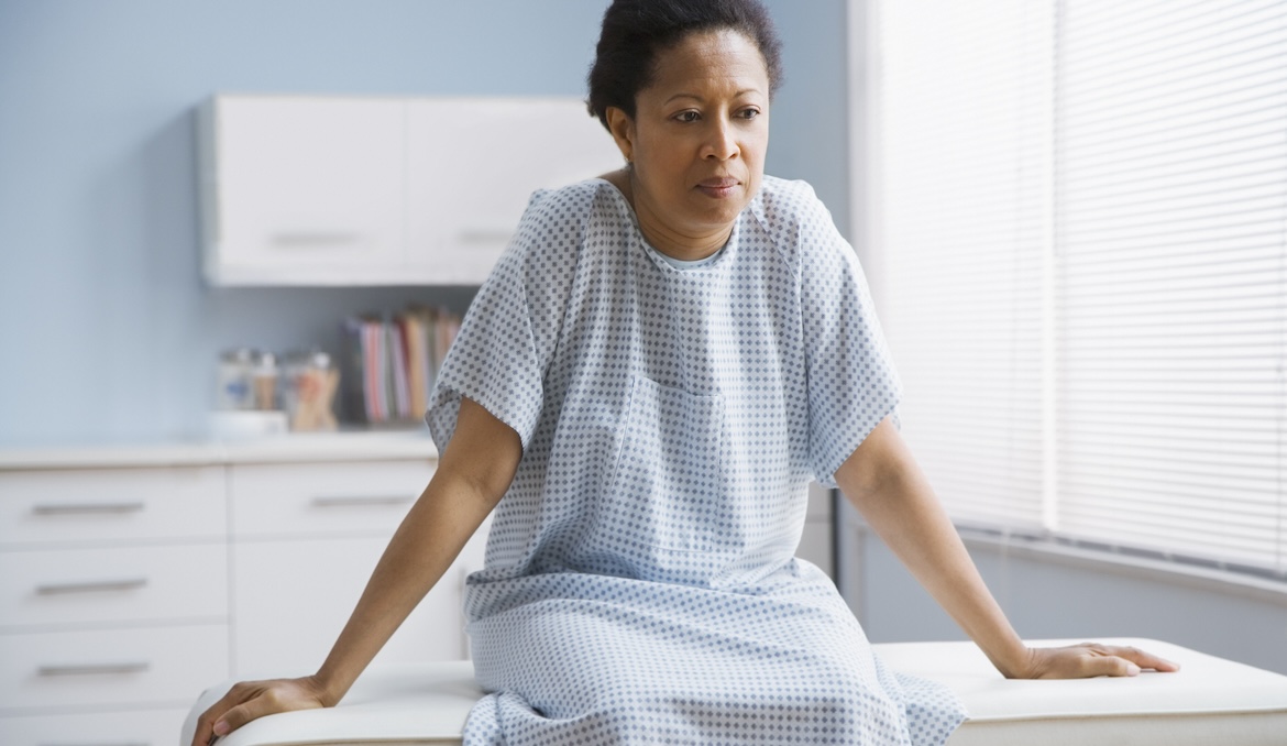 middle aged woman sitting on exam table at doctor's office wearing hospital gown