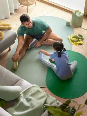 A man and child stretching on the floor on top of large, circular green exercise mats.