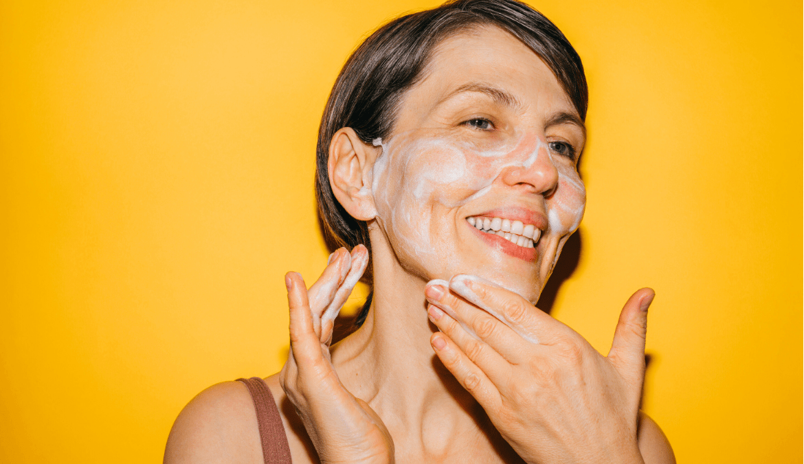 Smiling woman washing her face against a yellow backdrop