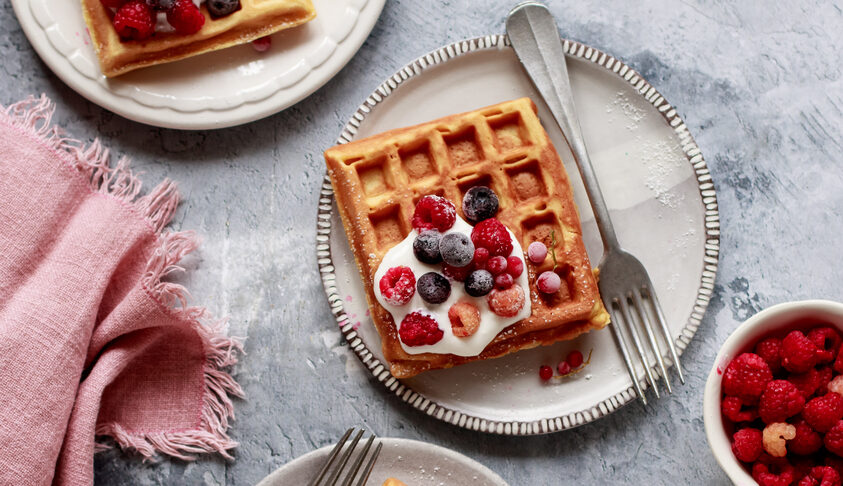 Several plates with kefir waffles and fruit on a kitchen table.
