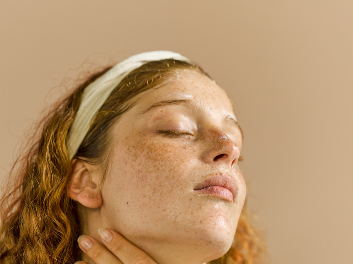 Woman applying skincare to her face with her eyes closed.