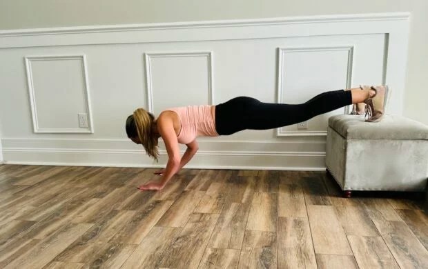 female PT with a blond ponytail wearing a tank top and leggings shows how to do decline push-ups correctly