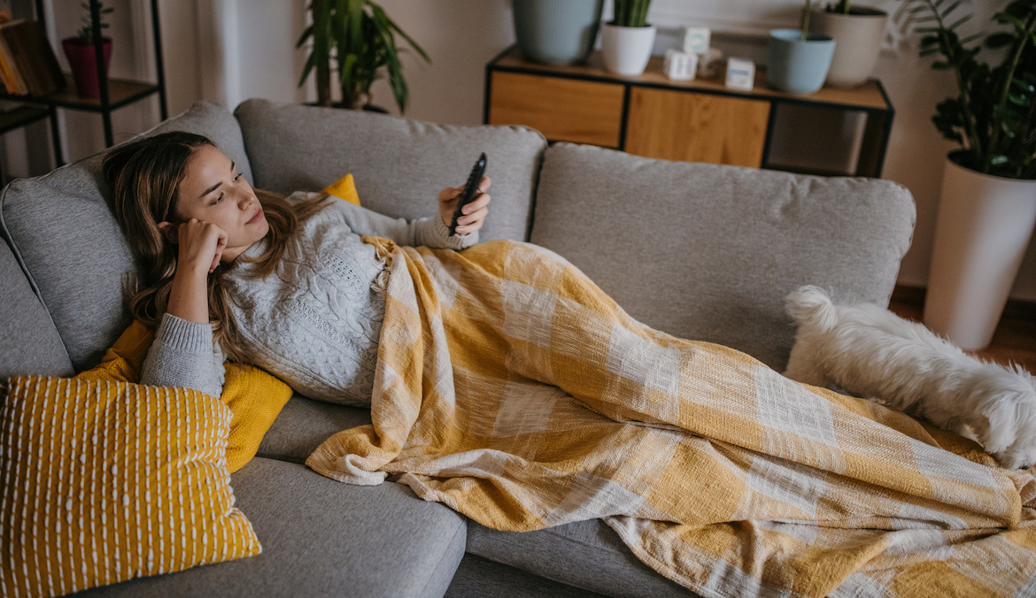 A person laying on the couch under a yellow blanket, feeling the effects of high cholesterol and fatigue