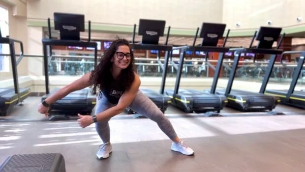 female trainer wearing glasses and smiling with long dark hair demonstrates how to do the gorilla walk exercise