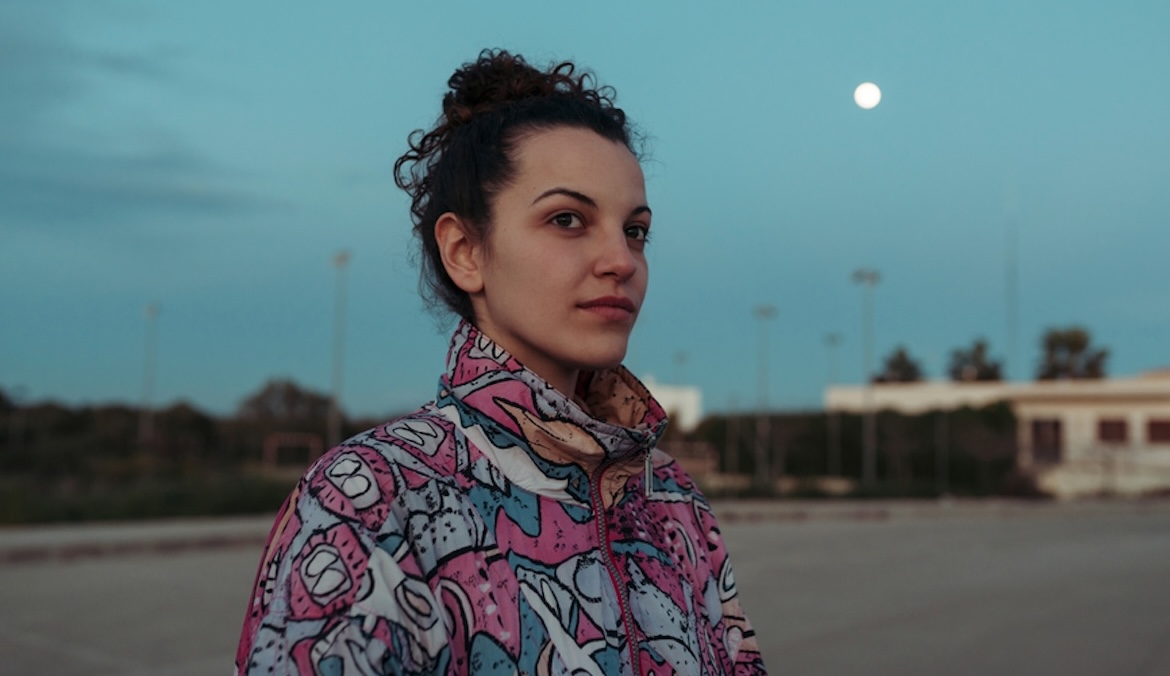 Portrait at dusk of a beautiful urban woman in the suburbs, with the moon in the sky behind.