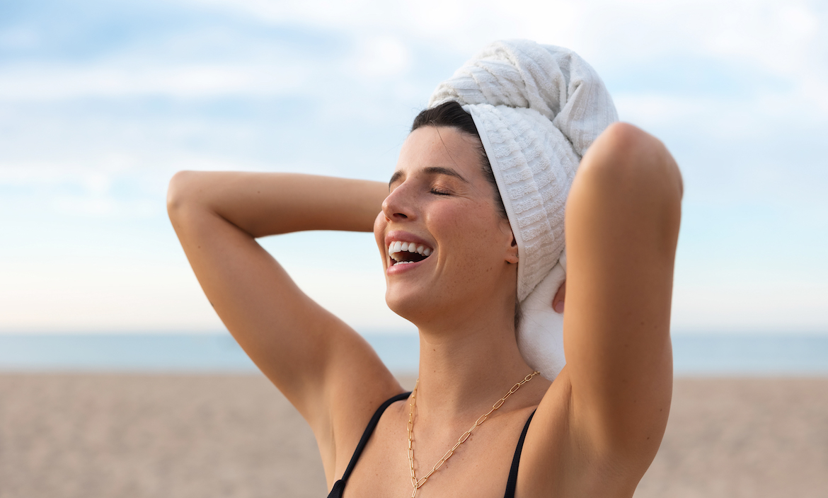 A woman on the beach with a towel wrapped around her hair.