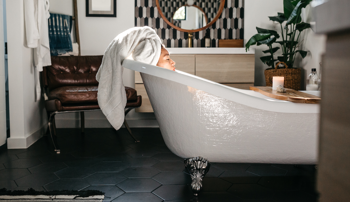 A woman with a towel wrapped around her head soaking in a claw-foot bathtub with eyes closed.