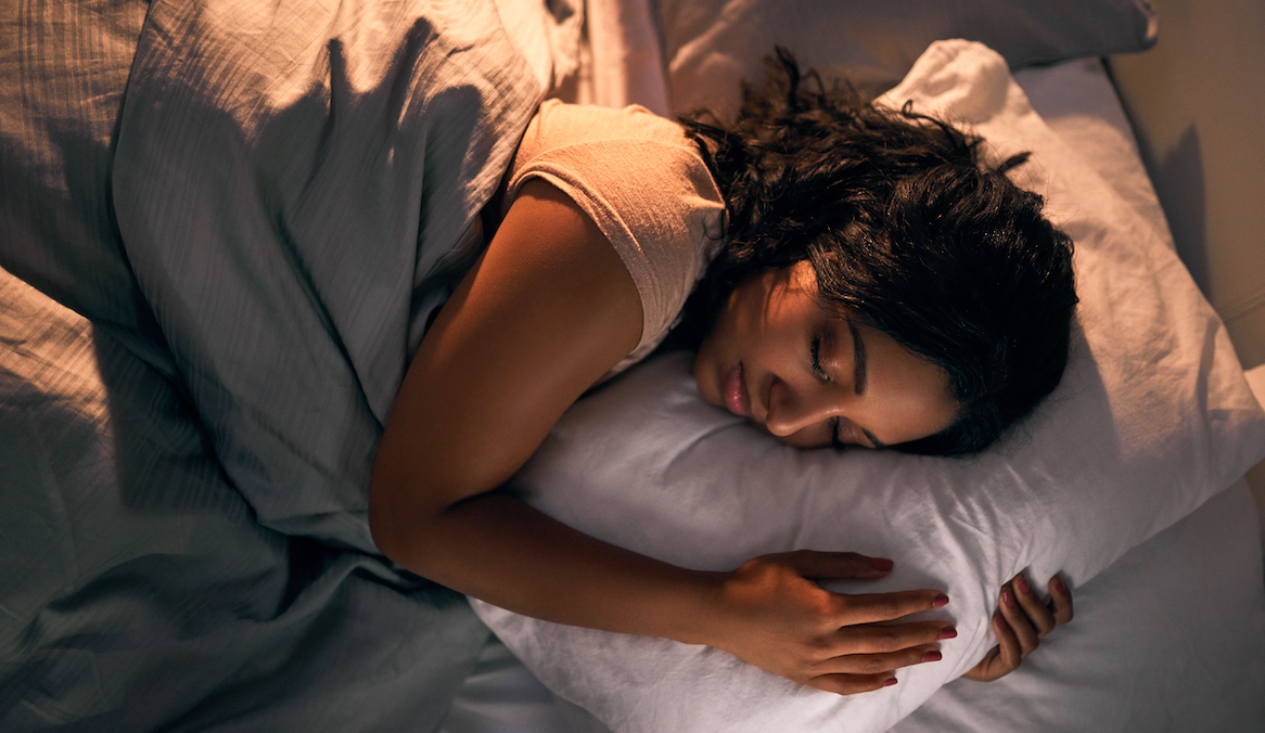 A woman lies in bed, clutching a bed pillow, symbolizing how to wash pillows.