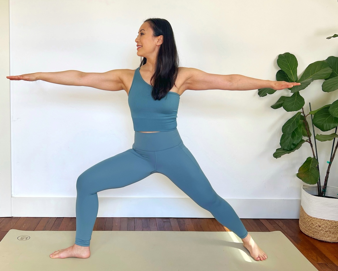 female yoga teacher with long dark hair shows correct form for yoga warrior 2 pose
