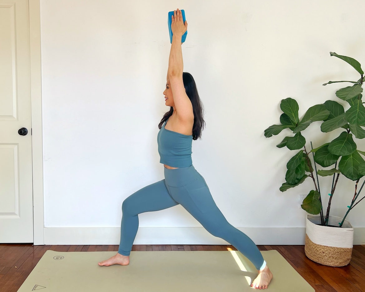female yoga teacher with long dark hair shows how to modify warrior 1 pose in yoga by using a block