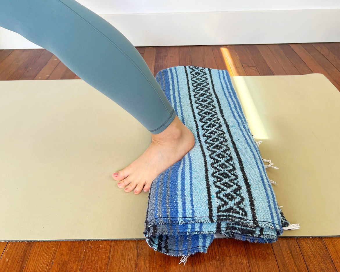 close up of a yoga instructor using a blanket under her back heel in warrior pose as a modification
