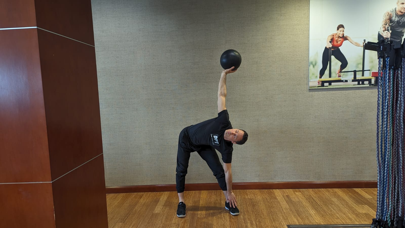 male personal trainer hold one hand up to the sky holding a heavy ball and one hand touches his toes