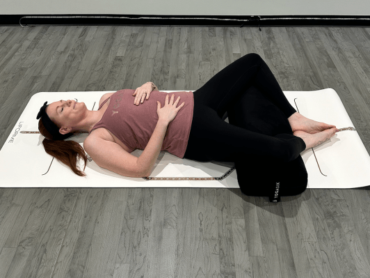 Yoga teacher demonstrating supine butterfly pose with bolster