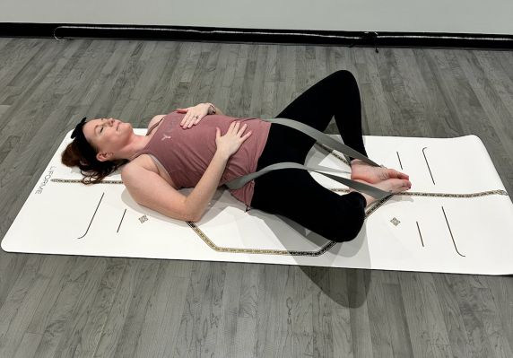 Yoga teacher demonstrating supine butterfly pose with strap