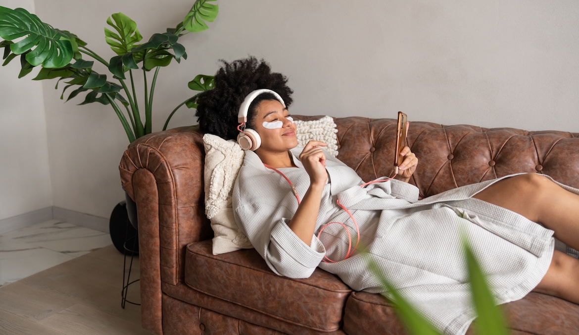 A woman wearing a bathrobe relaxes on a sofa while listening to music.