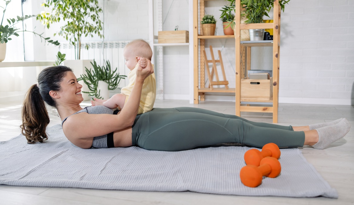 Photo of an active young mother doing a home workout and playing with her newborn