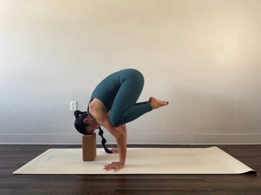 Yoga teacher demonstrating crow pose with block under forehead 