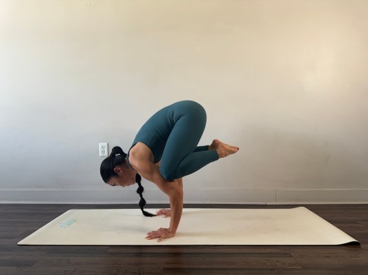 Yoga teacher demonstrating crow pose looking at hands