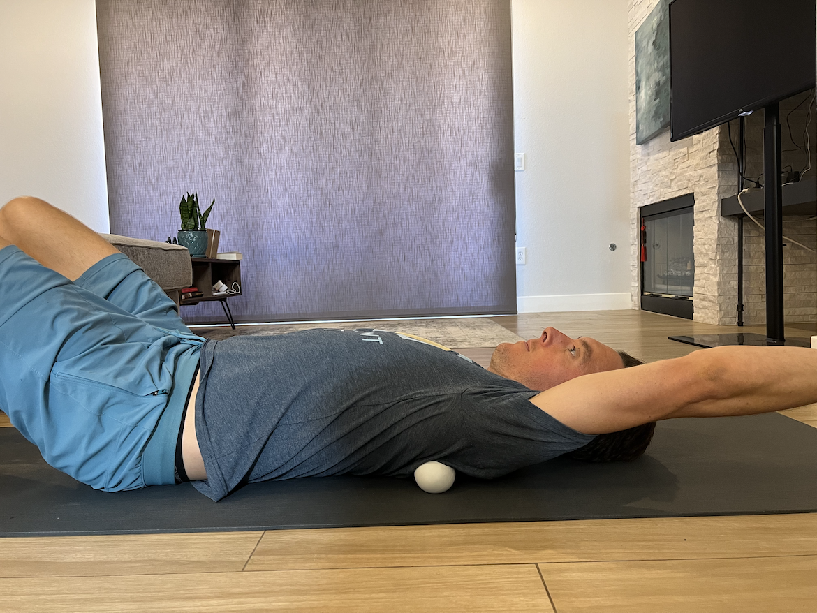 male physical therapist demonstrates how to use a lacross ball in a rotator cuff stretch
