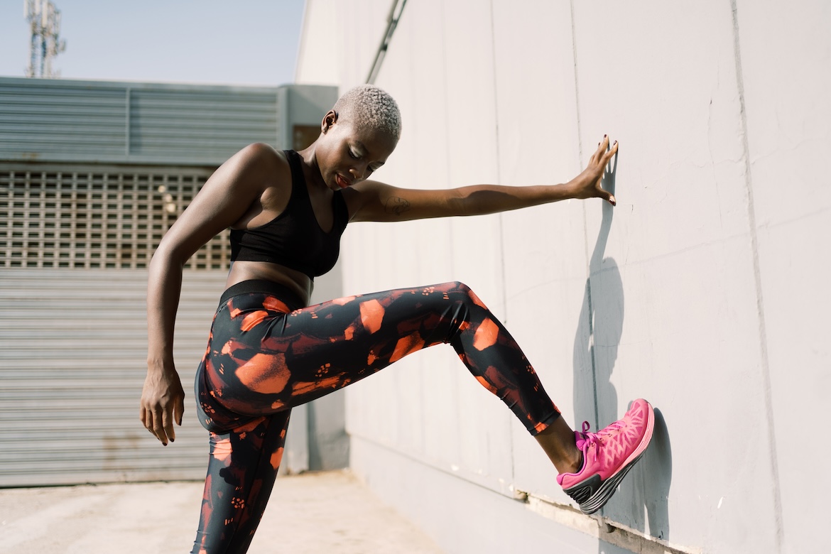 Side view of unrecognizable slim African American female athlete in stylish sportswear doing the best gluteus medius exercises against concrete wall of urban building