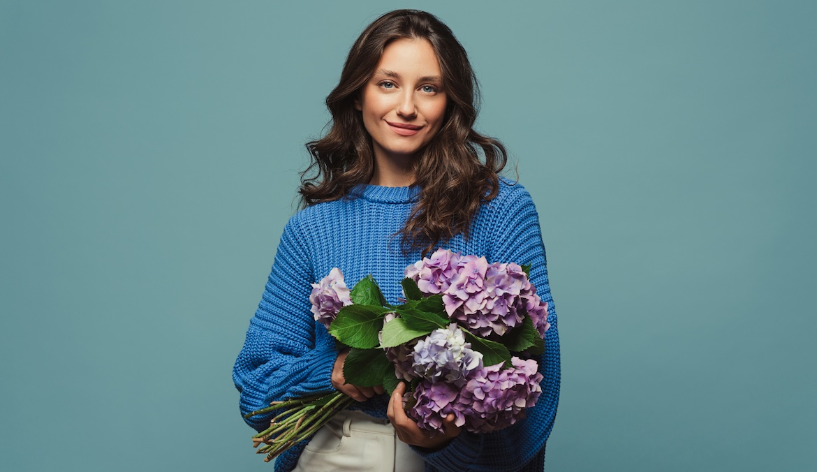 Portrait of a woman in a blue sweater holding a bouquet of hydrangea flowers in her hands