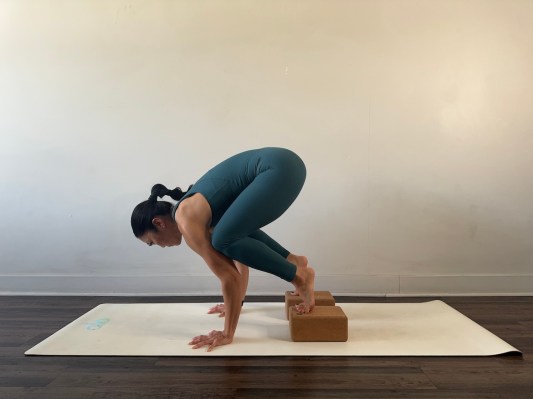 Yoga teacher demonstrating crow pose with block under feet