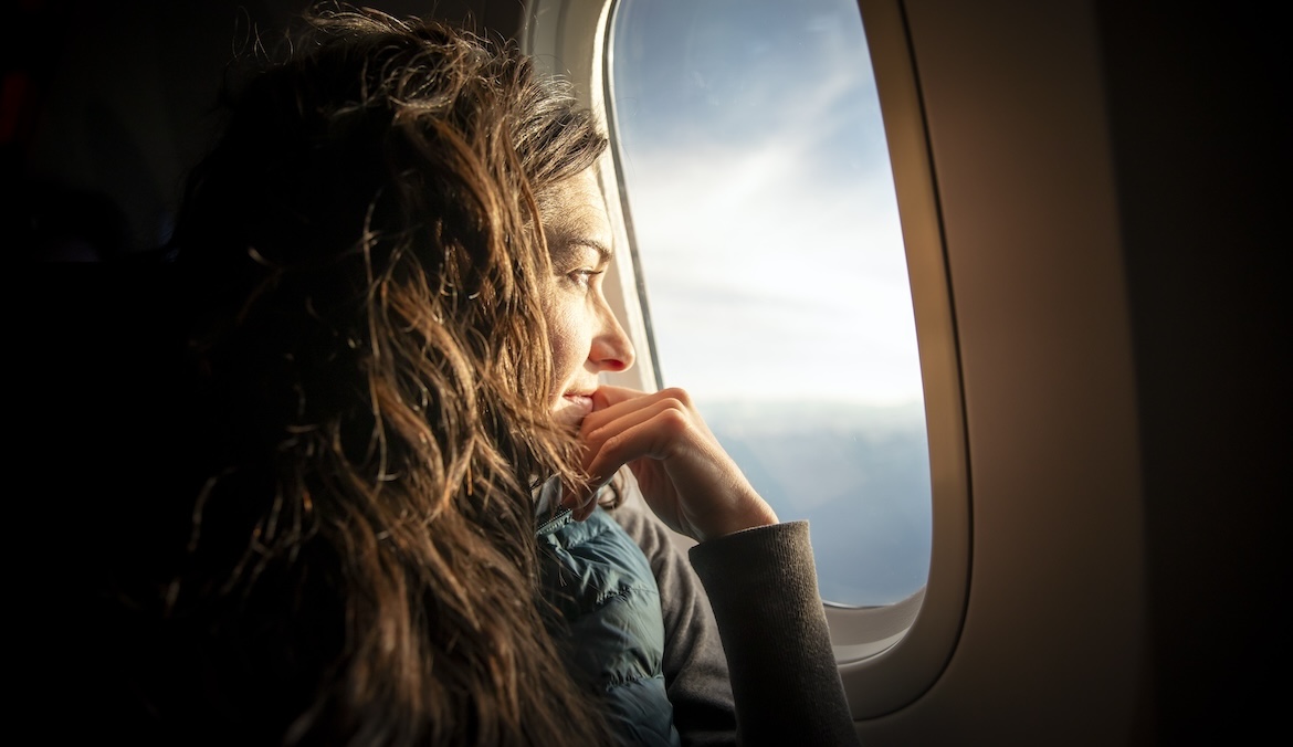 A woman looks out a plane window, symbolizing aerophobia.